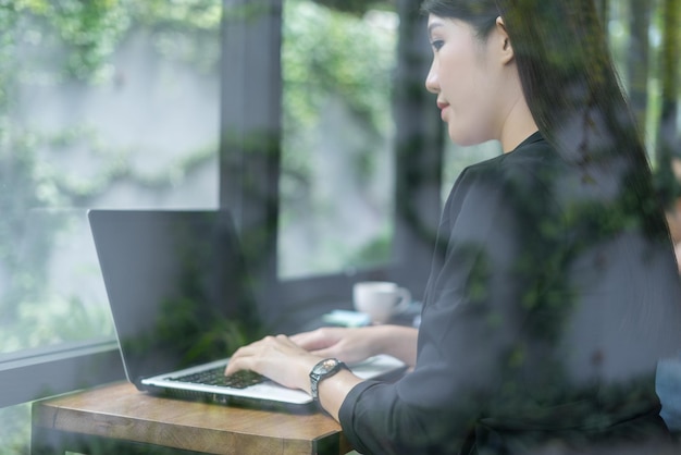 Businesswoman using laptop while sitting in office seen through window