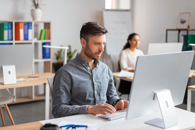 busy handsome millennial european man manager typing at computer at workplace in modern office interior