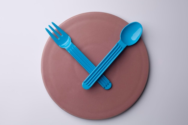 Clock pink plate with plastic spoon and fork eating time meal concept