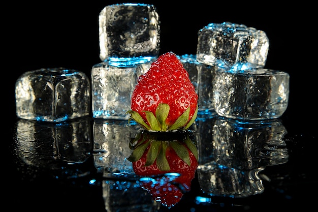 Close-up of fresh strawberry and ice with reflection on table against black background