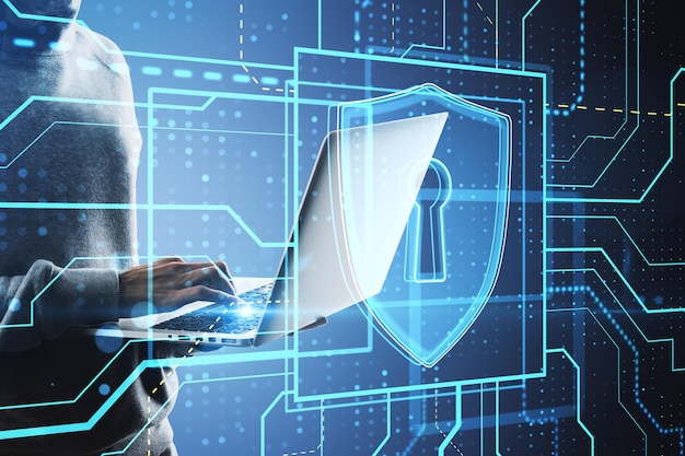 Close up of hacker hands using laptop with glowing safety and security circuit padlock shield hologram on blurry background Hacking and data theft concept Double exposure