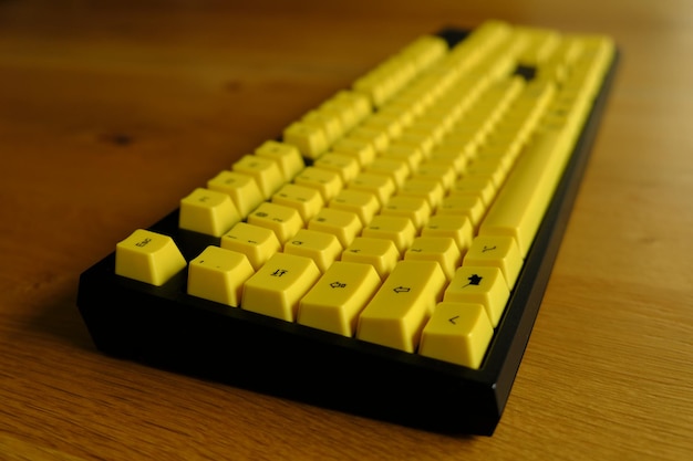 Close-up photo of a mechanical keyboard on a wooden table yellow key caps