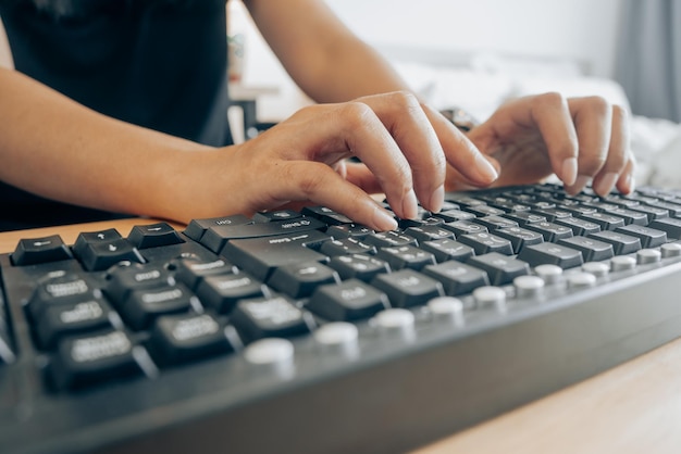 Close up shot of Asian woman's hands typing on old fashion keyboard while sitting at bedroom office