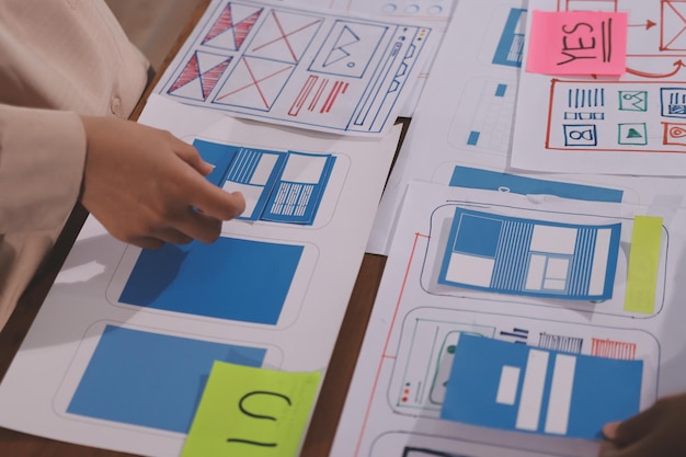 Close up ux developer and ui designer brainstorming about mobile app interface wireframe design on table with customer breif and color code at modern officeCreative digital development agency