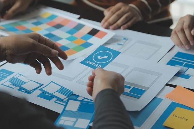 Close up ux developer and ui designer brainstorming about mobile app interface wireframe design on table with customer breif and color code at modern officeCreative digital development agency