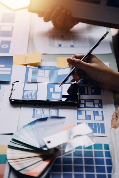 Close up ux developer and ui designer brainstorming about mobile app interface wireframe design on table with customer breif and color code at modern officeCreative digital development agency