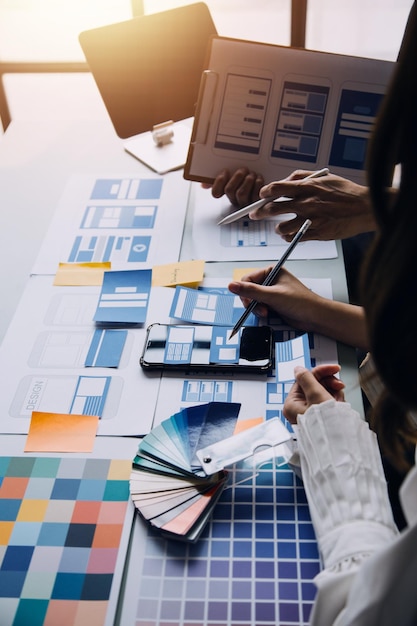 Close up ux developer and ui designer brainstorming about mobile app interface wireframe design on table with customer breif and color code at modern officeCreative digital development agency