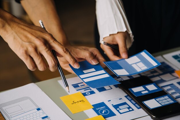 Close up ux developer and ui designer brainstorming about mobile app interface wireframe design on table with customer breif and color code at modern officeCreative digital development agency