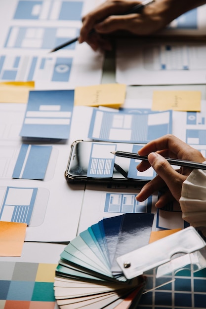 Close up ux developer and ui designer brainstorming about mobile app interface wireframe design on table with customer breif and color code at modern officeCreative digital development agency