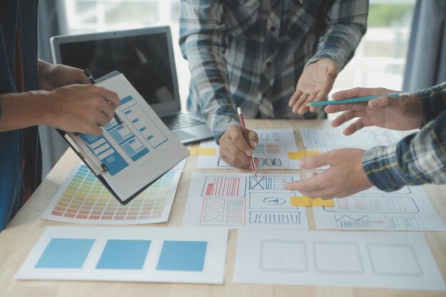 Close up ux developer and ui designer brainstorming about mobile app interface wireframe design on table with customer breif and color code at modern officeCreative digital development agency