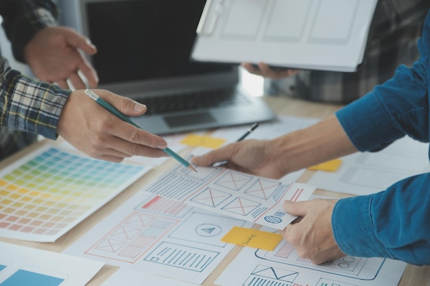 Close up ux developer and ui designer brainstorming about mobile app interface wireframe design on table with customer breif and color code at modern officeCreative digital development agency