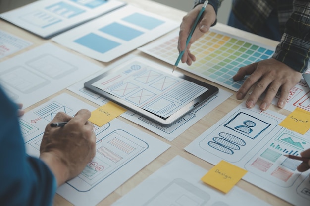 Close up ux developer and ui designer brainstorming about mobile app interface wireframe design on table with customer breif and color code at modern officeCreative digital development agency