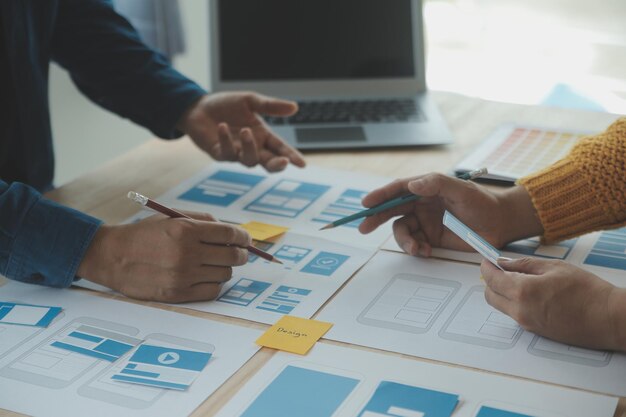Close up ux developer and ui designer brainstorming about mobile app interface wireframe design on table with customer breif and color code at modern officeCreative digital development agency