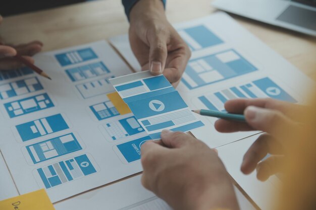 Close up ux developer and ui designer brainstorming about mobile app interface wireframe design on table with customer breif and color code at modern officeCreative digital development agency
