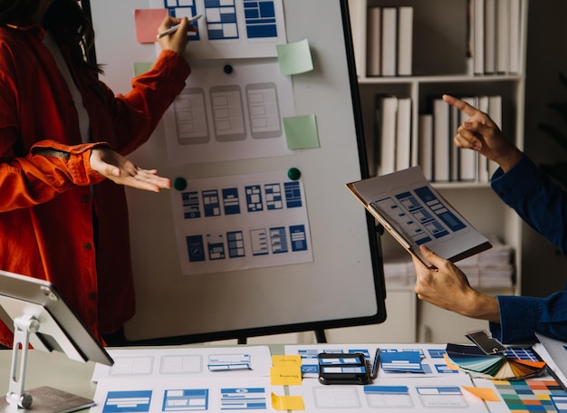 Close up ux developer and ui designer brainstorming about mobile app interface wireframe design on table with customer breif and color code at modern officeCreative digital development agency