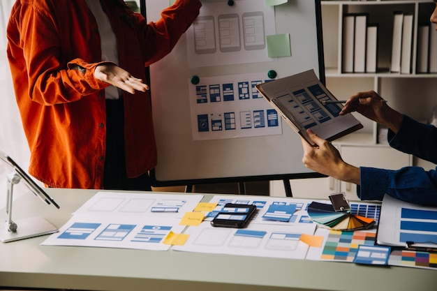 Close up ux developer and ui designer brainstorming about mobile app interface wireframe design on table with customer breif and color code at modern officeCreative digital development agency