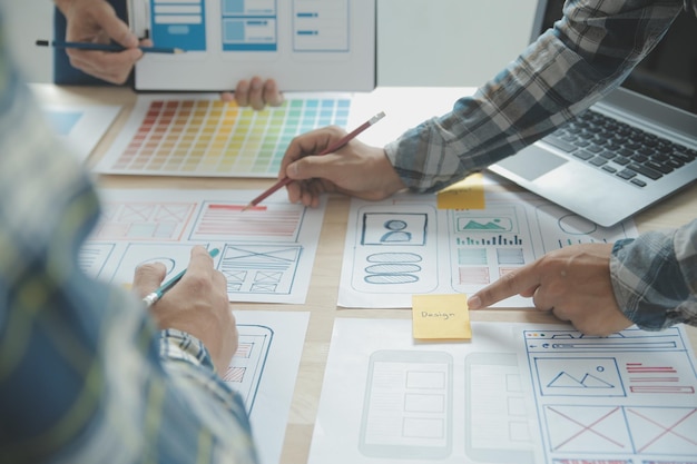 Close up ux developer and ui designer brainstorming about mobile app interface wireframe design on table with customer breif and color code at modern officeCreative digital development agency