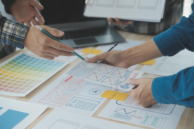 Close up ux developer and ui designer brainstorming about mobile app interface wireframe design on table with customer breif and color code at modern officeCreative digital development agency
