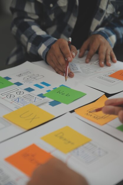 Close up ux developer and ui designer brainstorming about mobile app interface wireframe design on table with customer breif and color code at modern officeCreative digital development agency