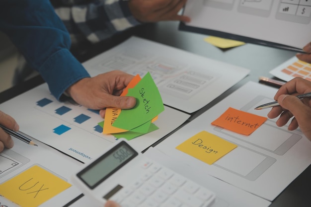 Close up ux developer and ui designer brainstorming about mobile app interface wireframe design on table with customer breif and color code at modern officeCreative digital development agency