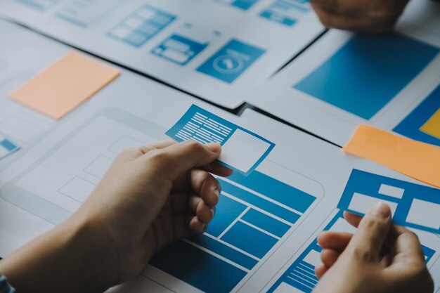 Close up ux developer and ui designer brainstorming about mobile app interface wireframe design on table with customer breif and color code at modern officeCreative digital development agency