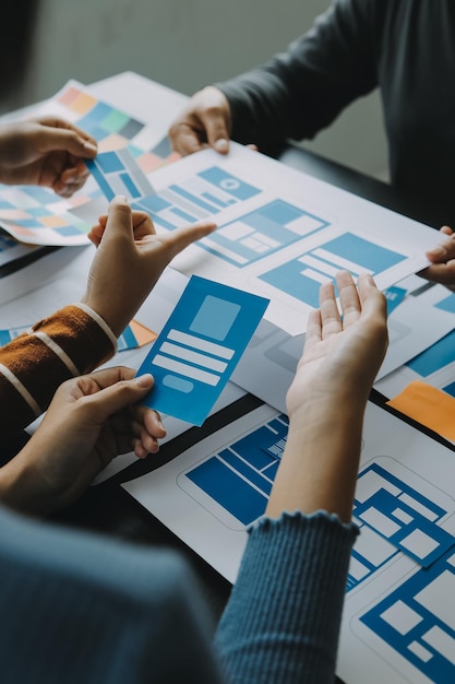 Close up ux developer and ui designer brainstorming about mobile app interface wireframe design on table with customer breif and color code at modern officeCreative digital development agency