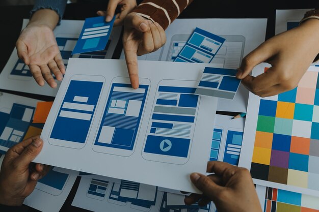 Close up ux developer and ui designer brainstorming about mobile app interface wireframe design on table with customer breif and color code at modern officeCreative digital development agency