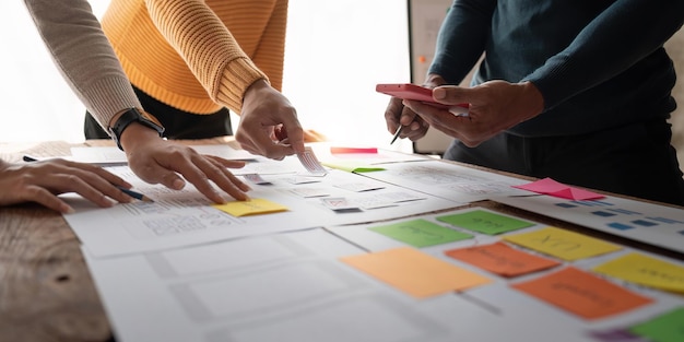 Close up ux developer and ui designer brainstorming about mobile app interface wireframe design on table with customer brief and color code at modern officeCreative digital development agencypanning