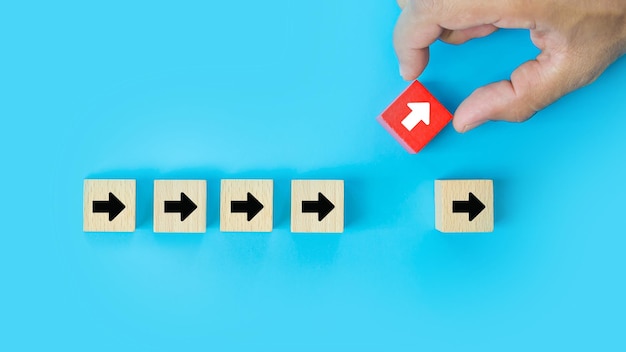Closeup hand choose cube wooden toy block stacked with arrow icon pointing to opposite directions for way of business change leader planning company and transform concept