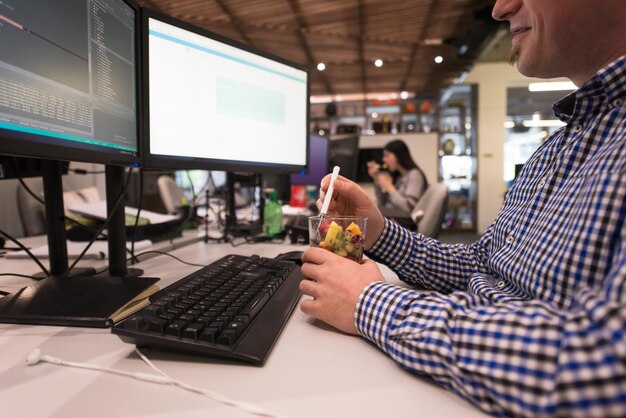 closeup of a young software developer eating a fruit salad from a clear cup at the startup office