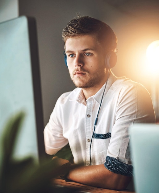 Computer music and web design with business man at desk in office for creative development Concentration headphones and streaming audio with serious employee in workplace for radio or research