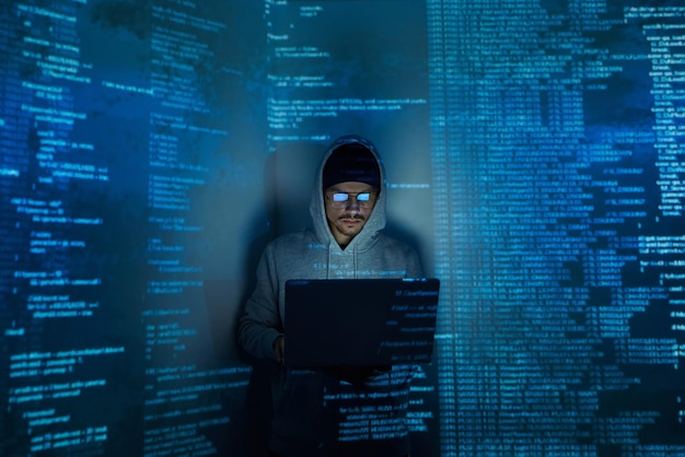 Confident young man in hooded shirt using computer while standing against dark background