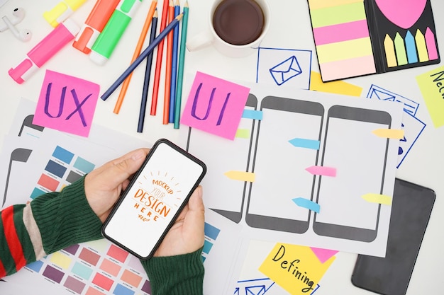 Creative UX UI designer hand holding mobile white screen mockup at working desk space White screen for graphic montage