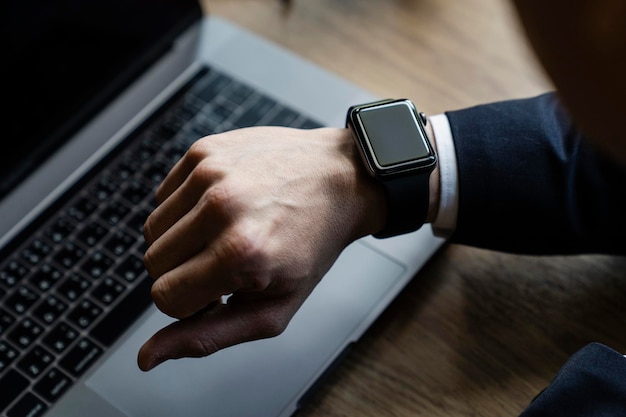 Cropped hand of man checking time against laptop