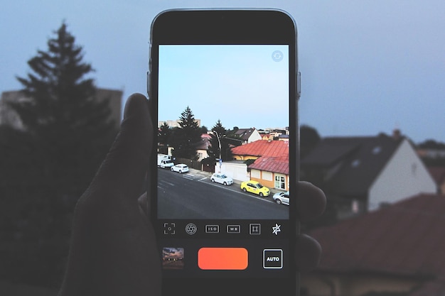 Cropped hand of person photographing cars and houses by using mobile phone