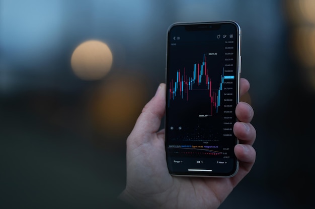 Cropped hand of trader holding mobile phone with graphs on screen