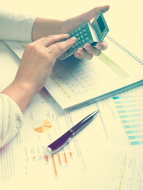 cropped hands of businesswoman using calculator with documents at desk