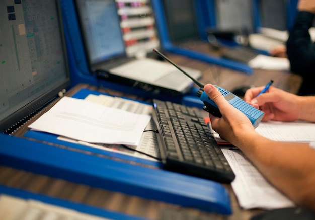 Cropped hands of engineer with walkie-talkie by computers at control room