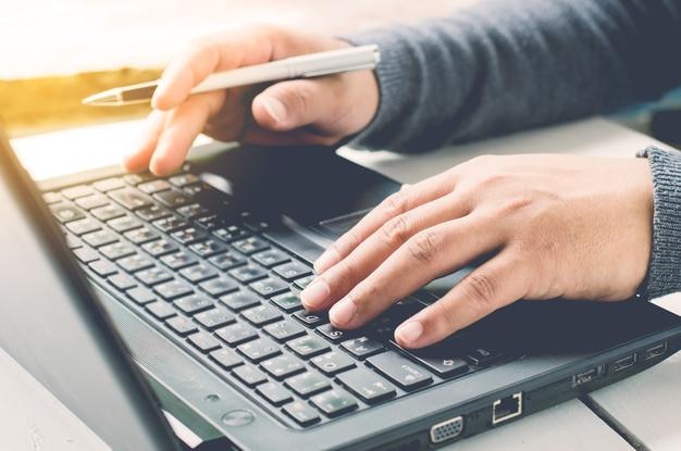 Cropped hands using laptop at table in office