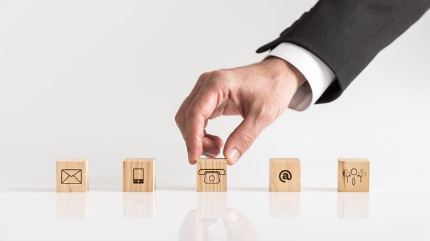 Cubes with contact symbols envelope at sign telephone and human icon being placed on a white table by a businessman conceptual of communication and customer support