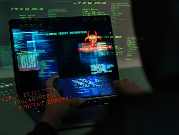Cybersecurity fraud and hands on a laptop and phone while programming or hacking a website Scam cyber attack and man hacker coding on a computer to steal information or data technology in the dark