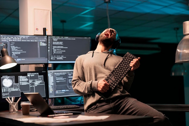 Database programmer playing guitar with keyboard, writing code with cloud computing and programming html source. Cheerful smiling developer having fun and acting silly in office.