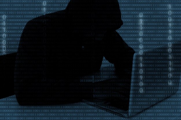 Digital composite image of hacker using computer with binary numbers
