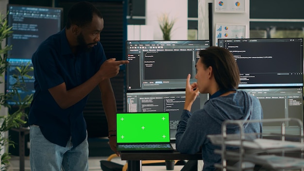 diverse app developers working with greenscreen on laptop and programming source code with html script on monitor. looking at isolated mockup template with chromakey display, copyspace.