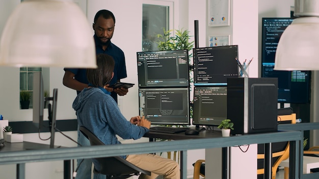 Diverse programmers collaborating on coding project compiling algorithm for new cloud computing user interface on computer monitors. Team of software engineers brainstorming ideas.