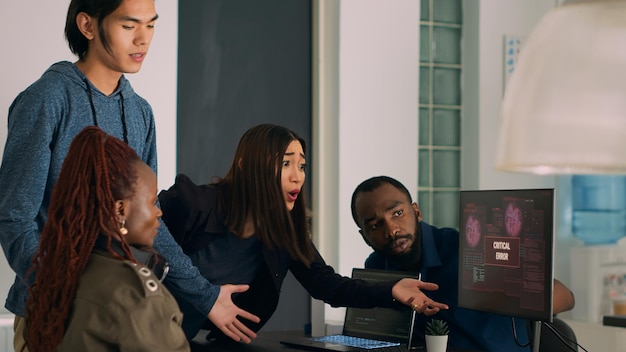 Diverse team of coders dealing with security breach alert on computer, trying to solve hacking and critical error. Engineers using terminal window and having system hacked crash.