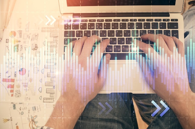 double exposure of mans hands typing over laptop keyboard and forex chart hologram drawing top view financial markets concept