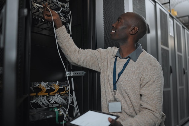 Engineer server room and black man with cable and tablet for database maintenance or software update Cybersecurity it or startup male coder on tech for programming or networking in data center