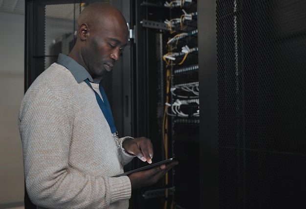 Engineer server room or black man with tablet for database connection cable maintenance or software update at night Cybersecurity IT and male coder with technology for networking in data center