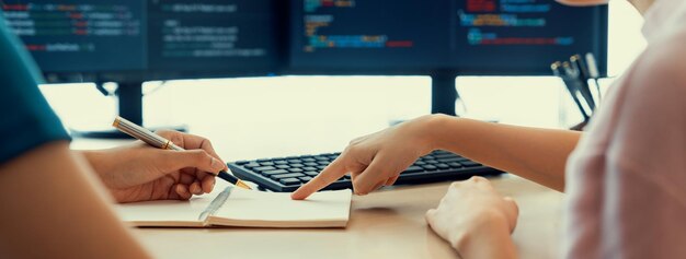 Female programer taking a note while young skilled web developer present program while computer displayed program code at modern office company Java script web design concept Burgeoning